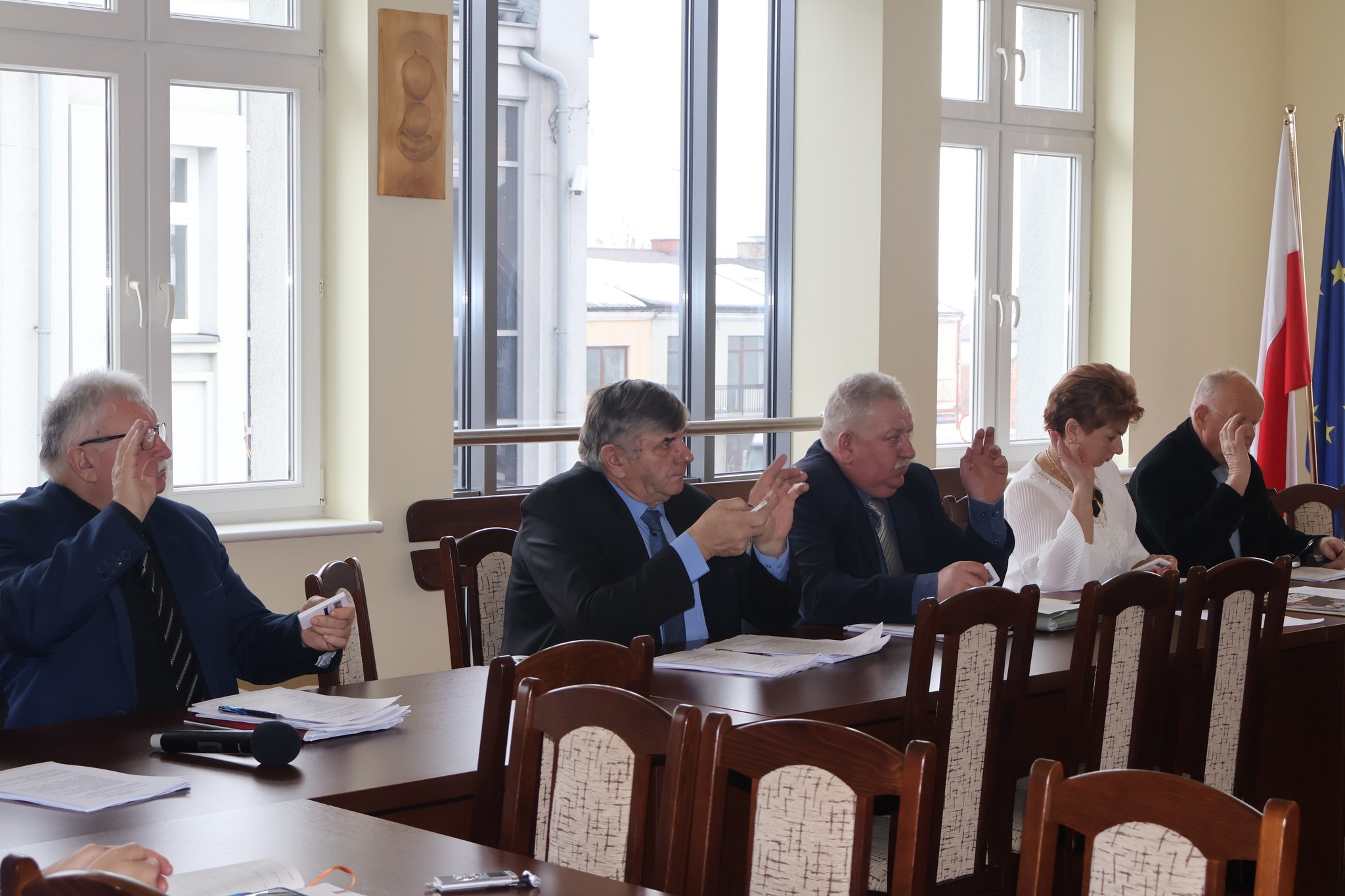 Na zdjęciu grupa radnych siedzących przy stole i głosujących za projektem 