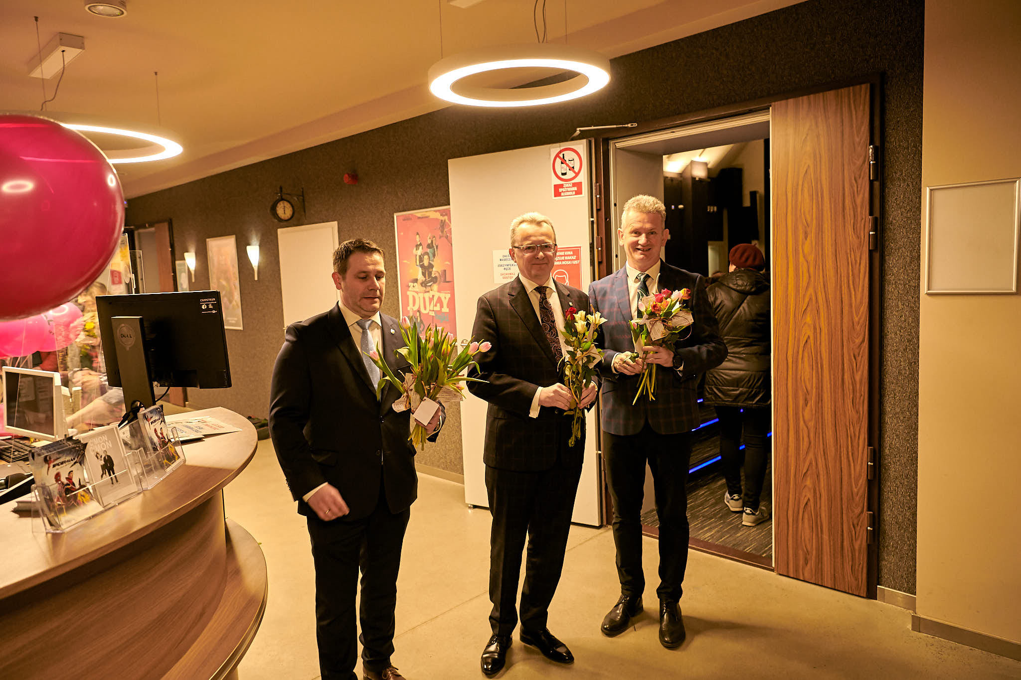 Z-ca burmistrza Grzegorz Molendowski, burmistrz Arkadiusz Sulima oraz sekretarz gminy Mirosław Chołuj trzymają w rękach kwiaty przygotowane dla Pań, które przychodzą na koncert.