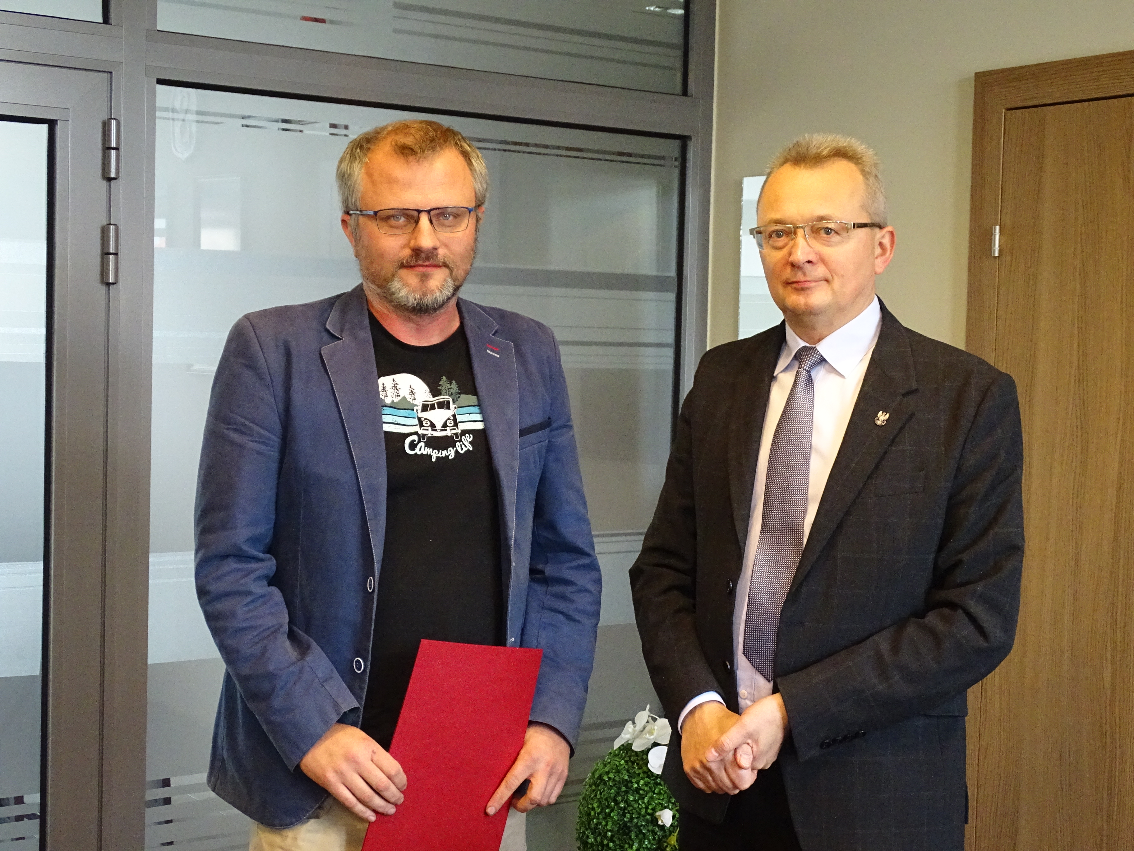 Burmistrz Zwolenia Arkadiusz Sulima wręczył wykonawcy podpisaną umowę. Na zdjęciu 2 mężczyzn, jeden z nich trzyma w ręce czerwoną teczkę