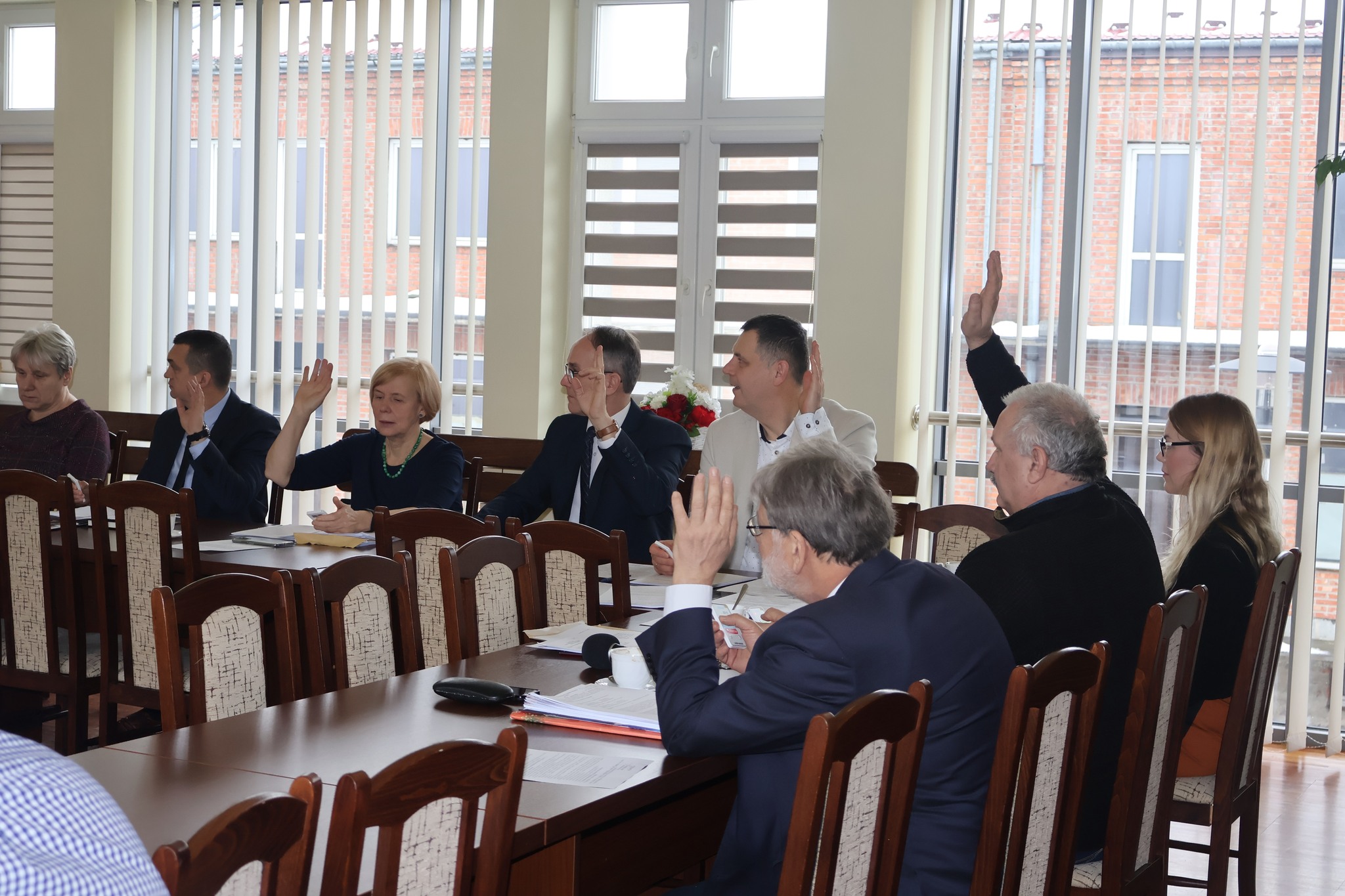 Na zdjęciu grupa radnych siedzących przy stole i głosujących za projektem 