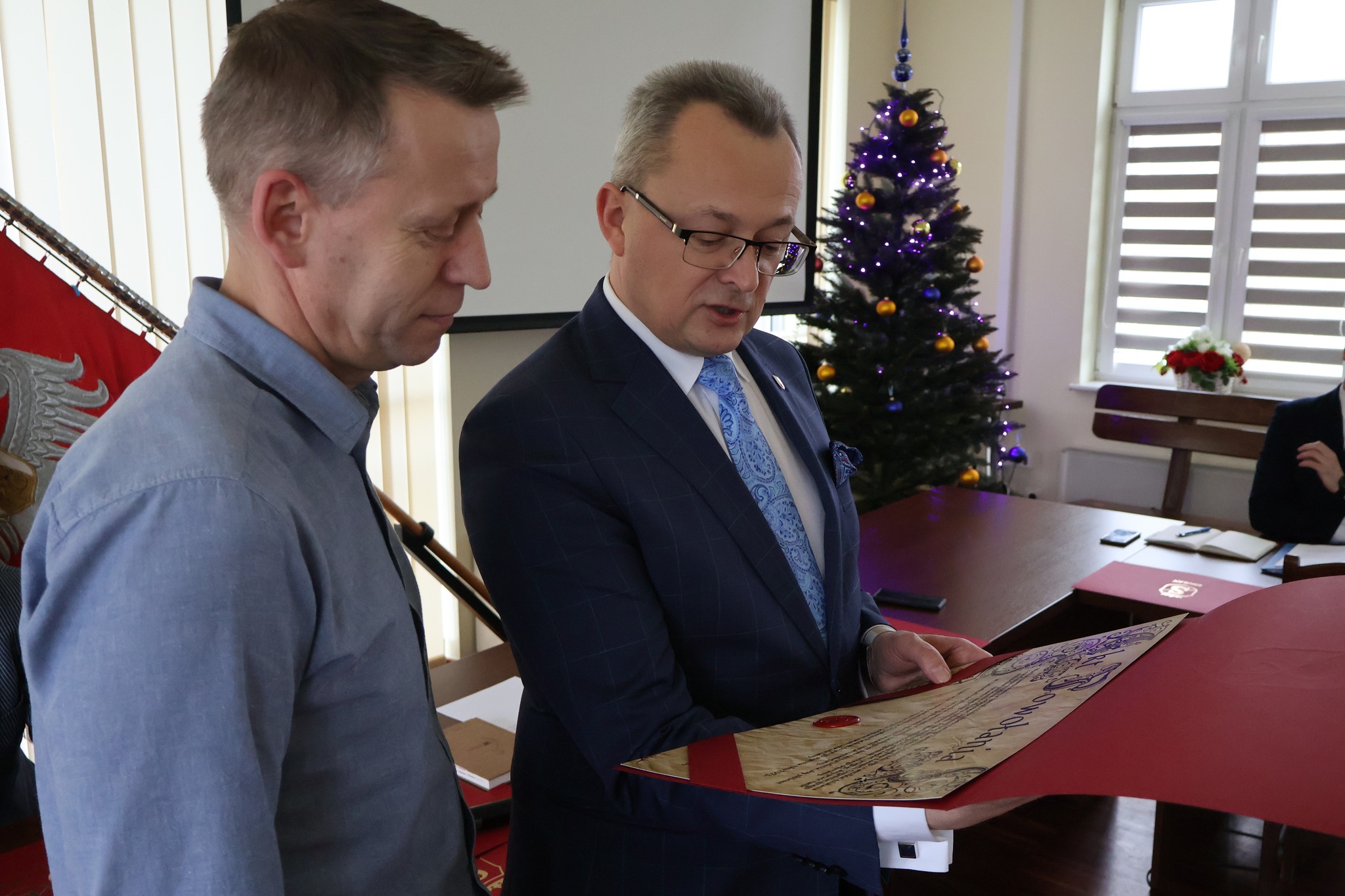 Na zdjęciu jest dwóch mężczyzn trzymających w dłoniach akt powołania
