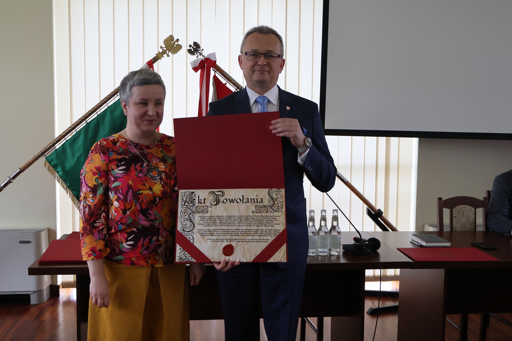 Na zdjęciu są dwie osoby - kobieta i mężczyzna - trzymają w dłoniach akt powołania.
