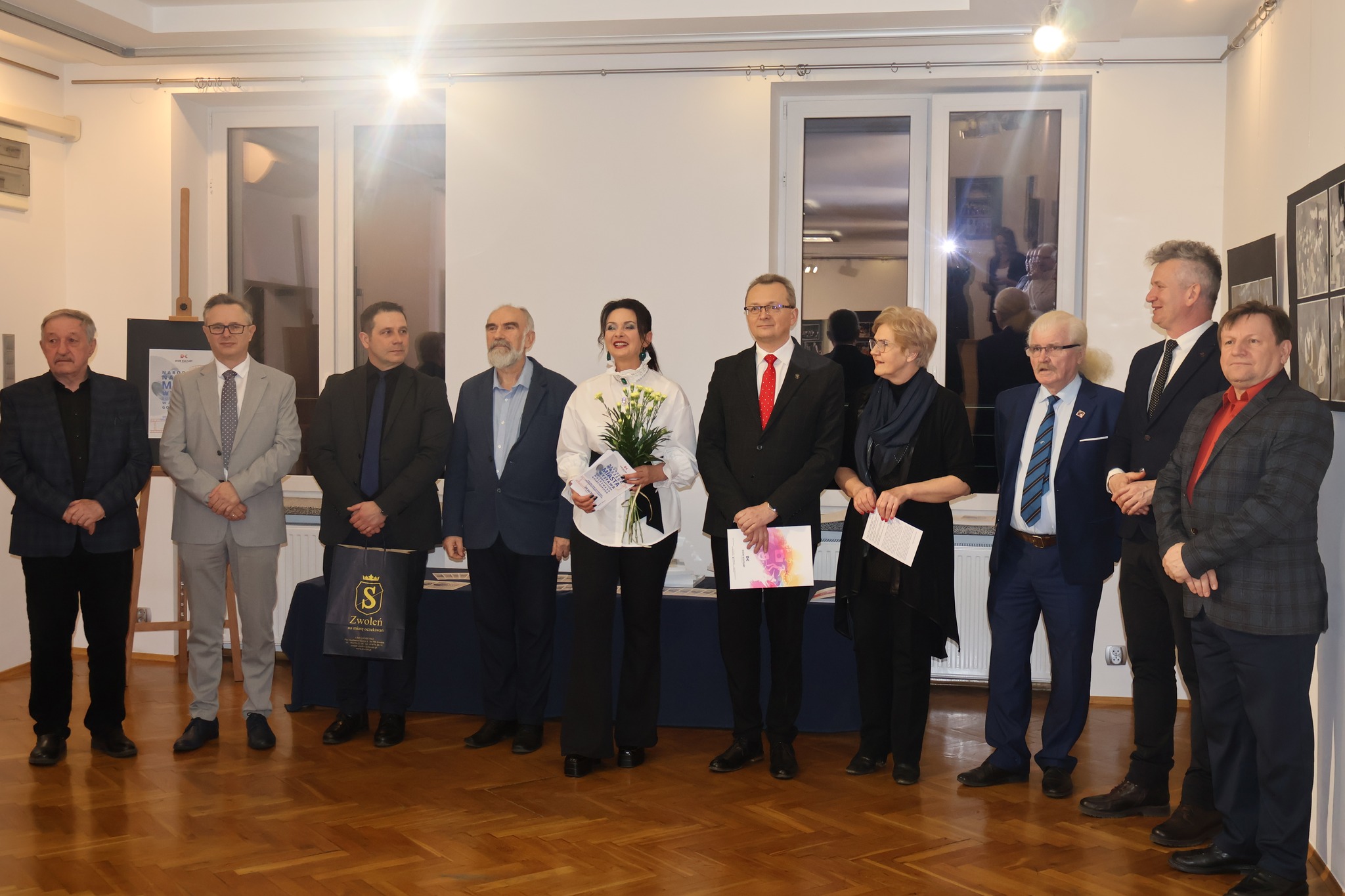 Zdjęcie z oficjalnego otwarcia wystawy. Na zdjęciu jest 10 osób, które stoją na środku sali wystawowej, wśró nich znajdują się dwie kobiety.