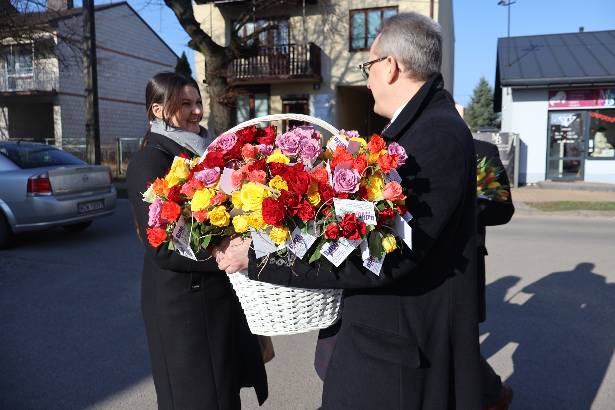 Burmistrz z koszem róż wręcza kwiat napotkanej na ulicy pani